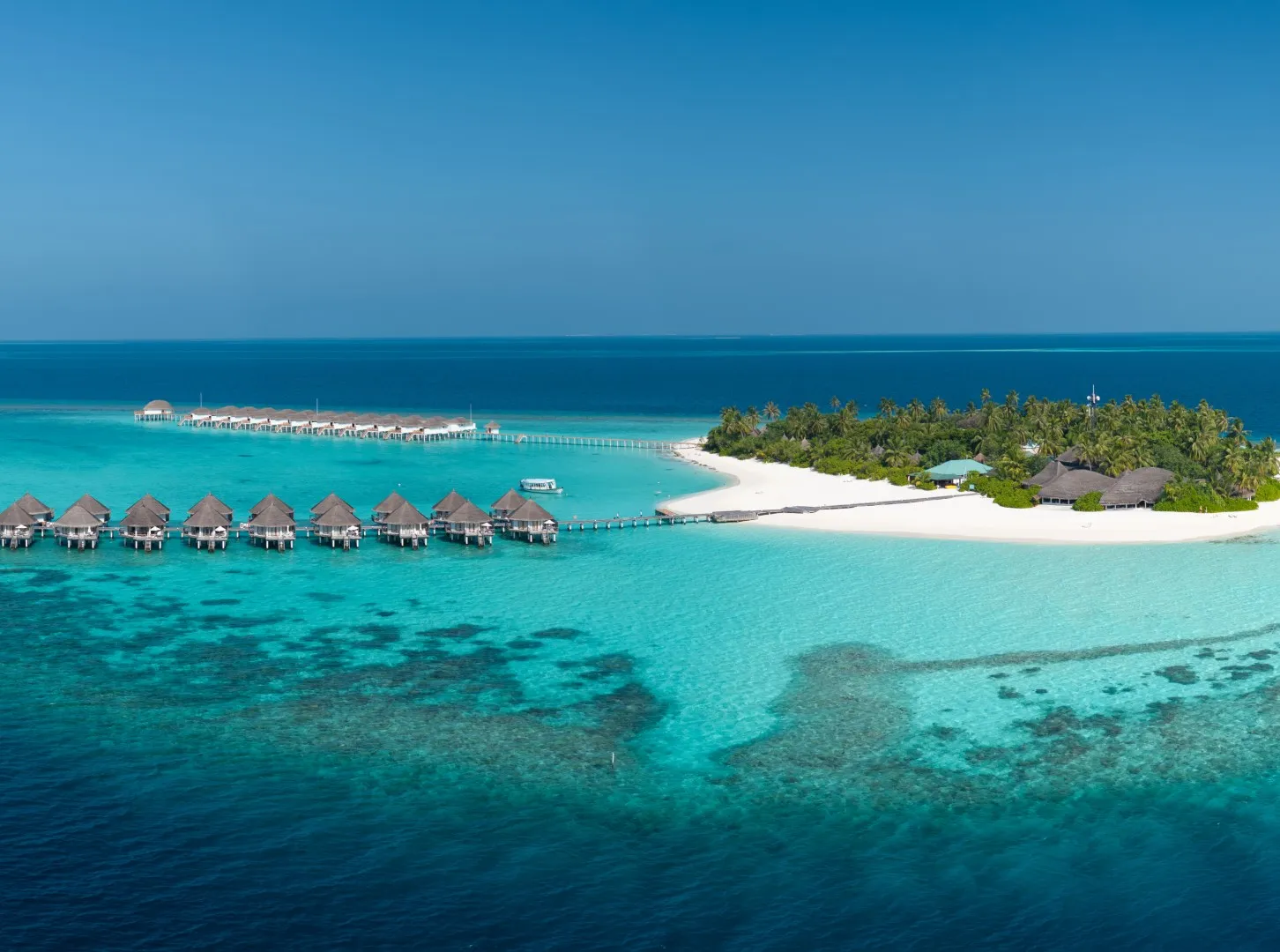 L’isola dall’alto, con la fila dei bungalow sull’acqua sulla laguna a sinistra e il reef scuro sotto la superficie.