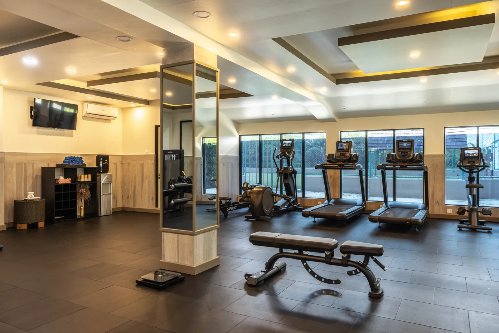 The gym with its treadmills, bench and weights in front of the windows.