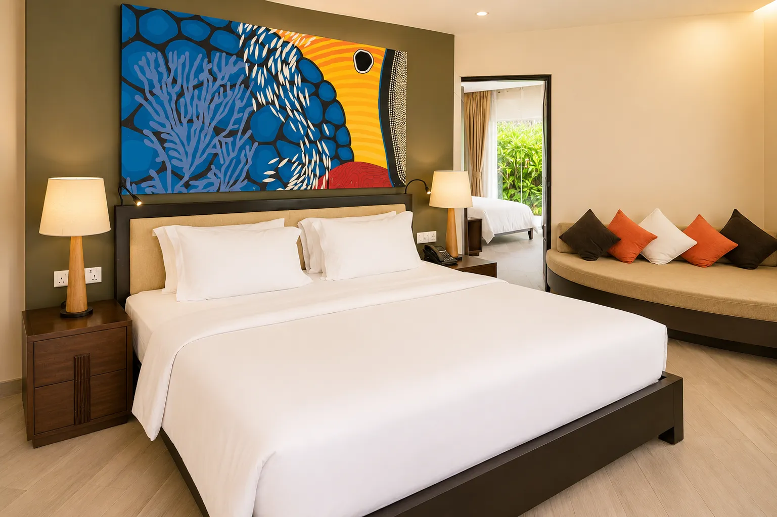 A family villa bedroom, with its king bed, a sofa with orange cushions and a coral painting above the bed.