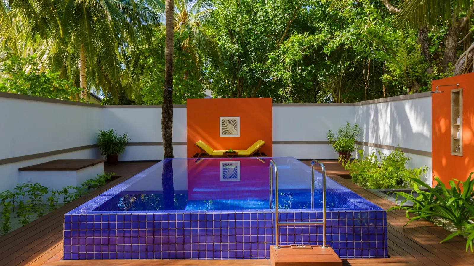 A Deluxe Beachfront Pool Villa’s private pool, with blue tiles, a timber deck and the orange wall.