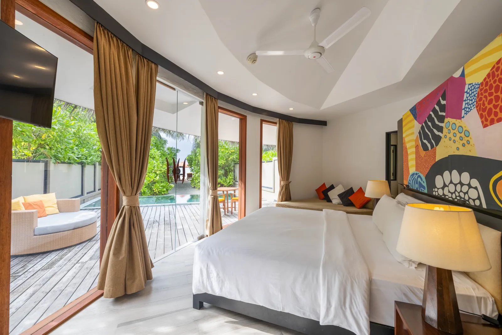 A family villa’s king bed, the bright painting and the door open to the veranda and the garden.