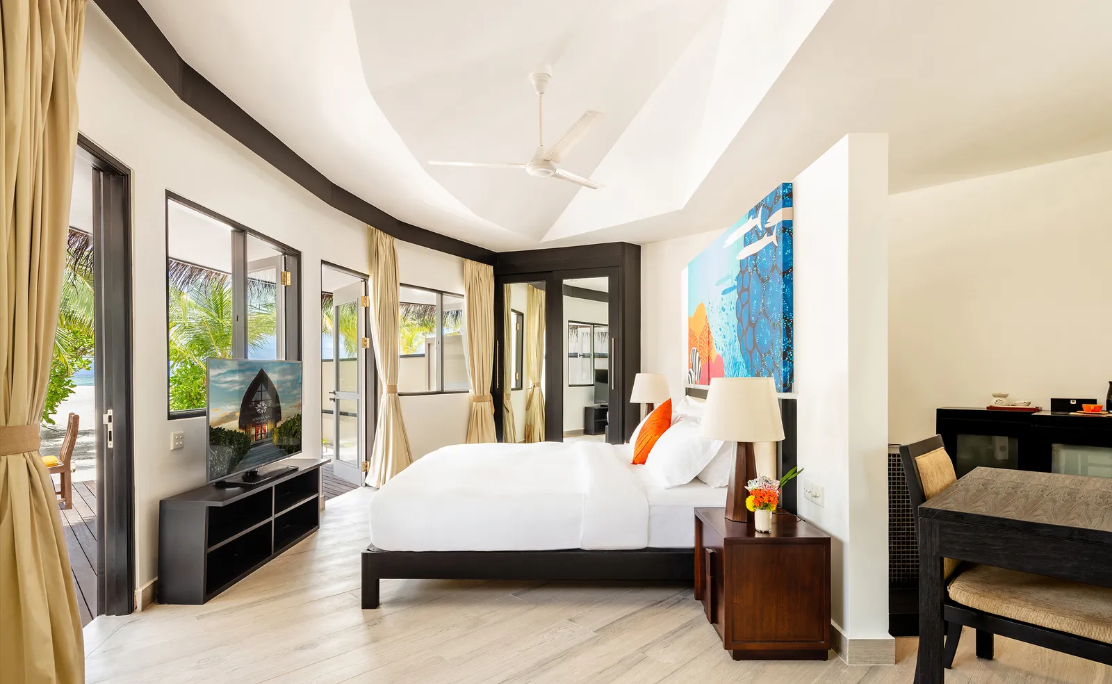 A beach villa bedroom, with its king bed, a large bright painting and the French window to the garden.