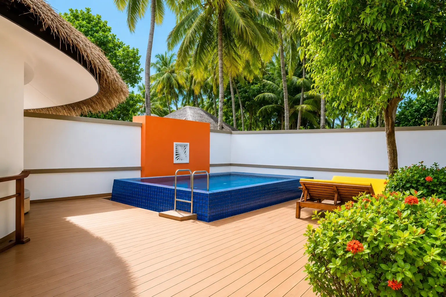 The pool deck of the Velavaru Two-Bedroom Pool Villa, with loungers, the orange wall and red flowers.