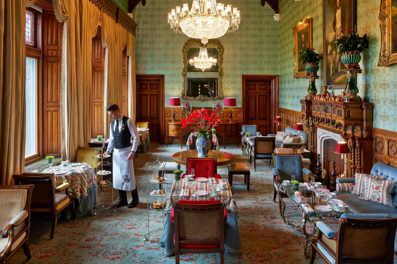 Tables laid for tea among floral sofas and green panelling