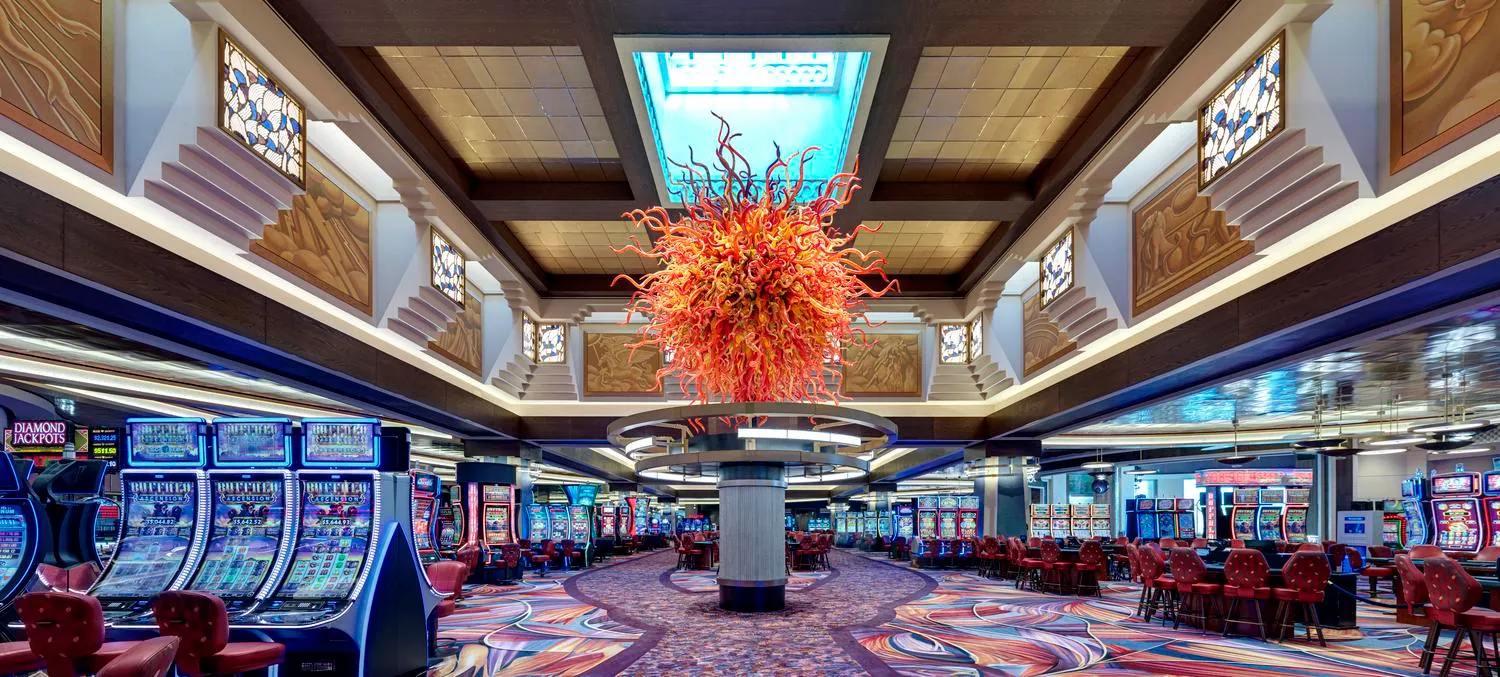 The casino floor, with rows of slot machines and tables beneath a large red and orange glass sculpture hung from the ceiling.