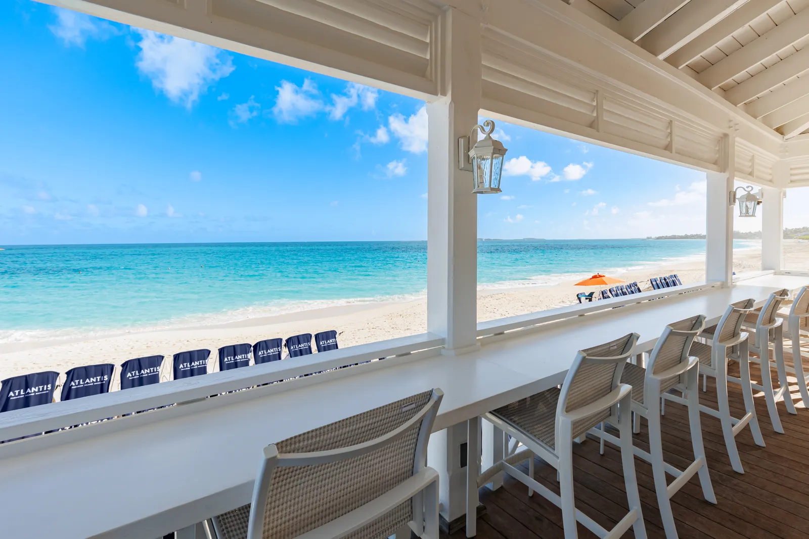 The white wooden counter of a beach bar, its stools facing the sand, blue loungers and the sea.