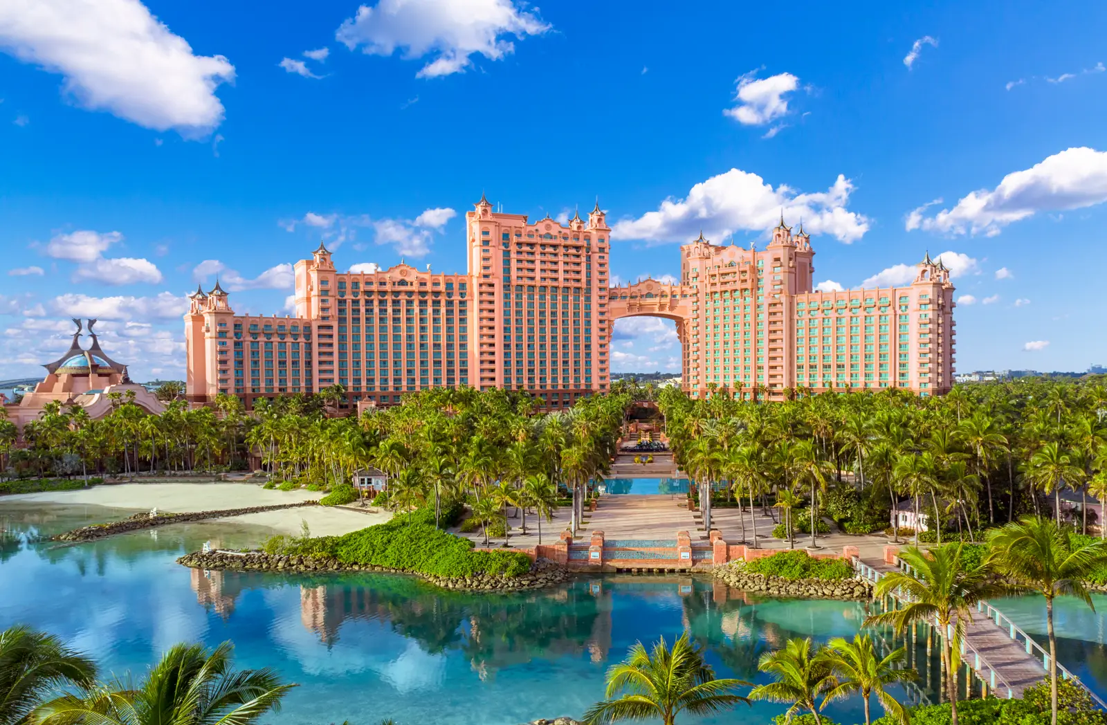 The 2 pink towers of The Royal, joined by a bridge high above the ground, over palm trees and a calm lagoon.