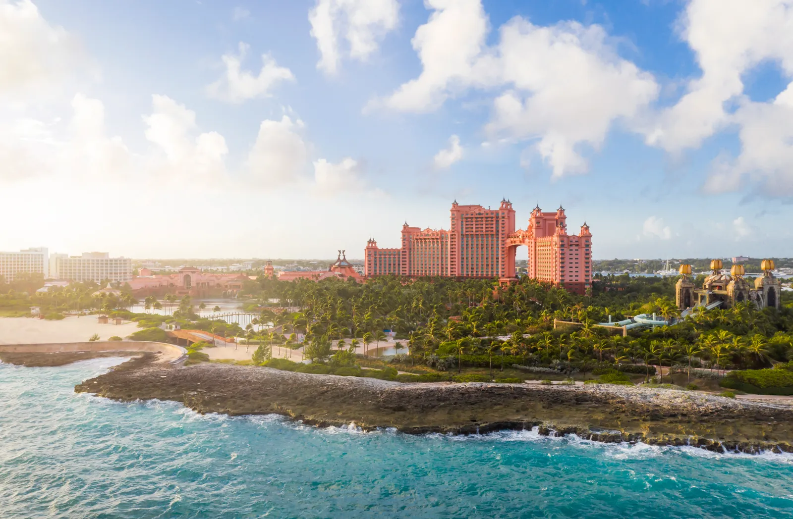 The rocky shore of Paradise Island early in the morning, with The Royal’s towers above the palms and waves in the foreground.