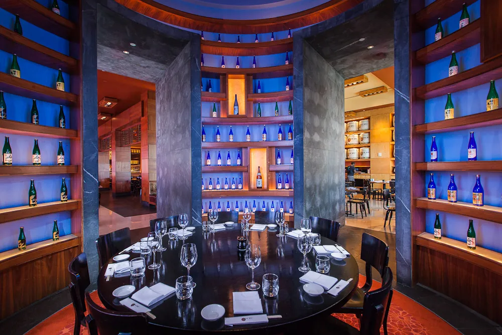 Il tavolo rotondo nella sala del sake di Nobu, fra pareti di bottiglie illuminate di blu.