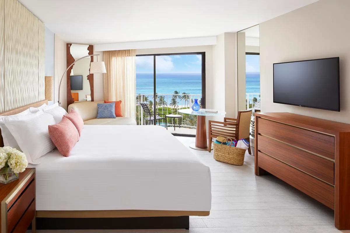 A room at The Coral with a king bed, a pale floor and a balcony over palms and the sea.