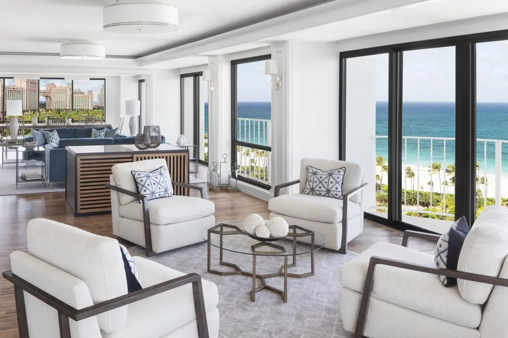 The living room of The Coral’s penthouse, with white armchairs and dark-framed glazed doors onto the beach and the sea.
