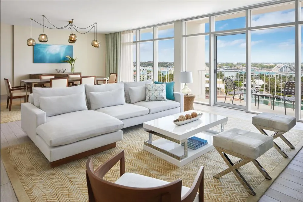The living room of a Presidential suite at The Coral, with a white sofa, a dining area and windows onto the harbour.