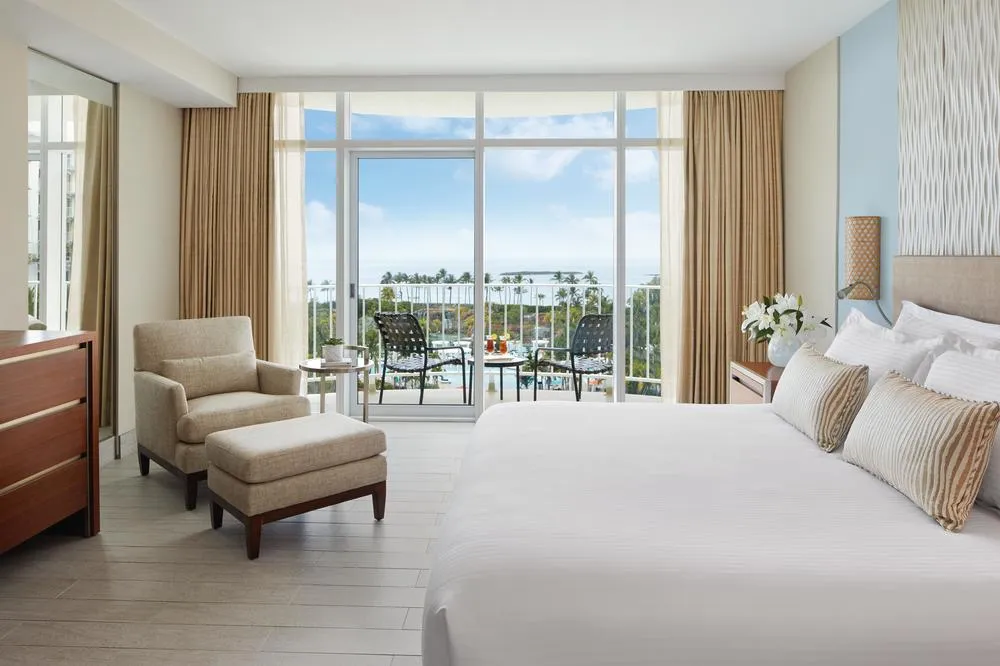 The bedroom of a Regal suite at The Coral: a king bed, an armchair with a footstool and a balcony over gardens and sea.
