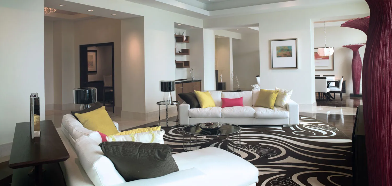 The living room of a Presidential suite at The Cove, with white sofas, yellow cushions and a black and white swirled rug.