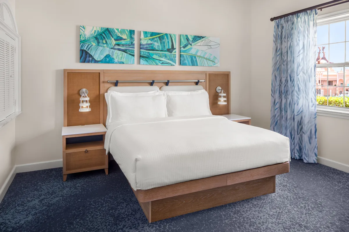 The bedroom of a villa at Harborside, with a king bed, a timber headboard and 3 paintings of green leaves on the wall.