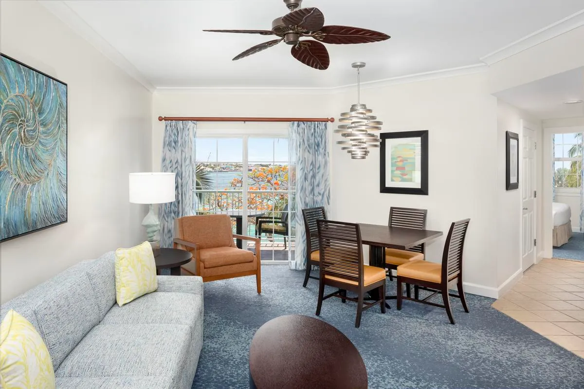 The living room of a villa at Harborside with a dining table, a large blue painting and a glazed door towards the marina.