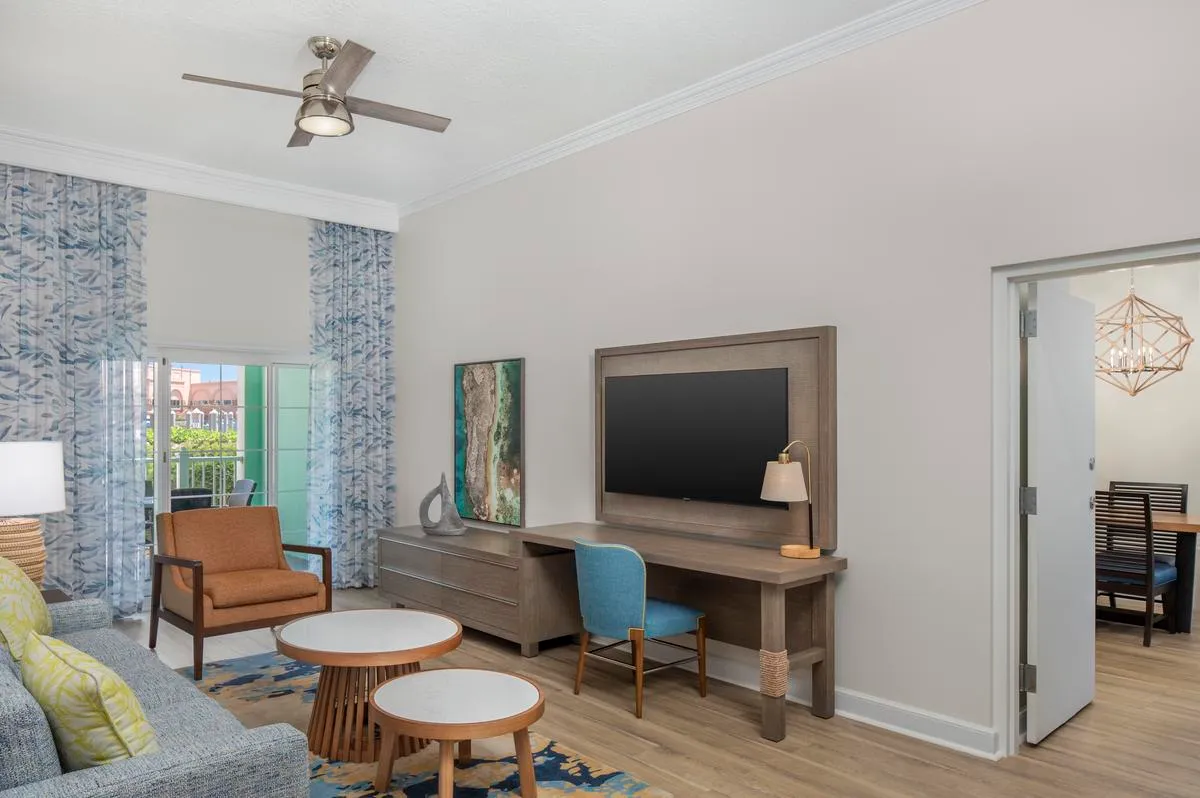 The living room of a villa at Harborside, with a grey sofa, tan armchairs, a desk and a ceiling fan.