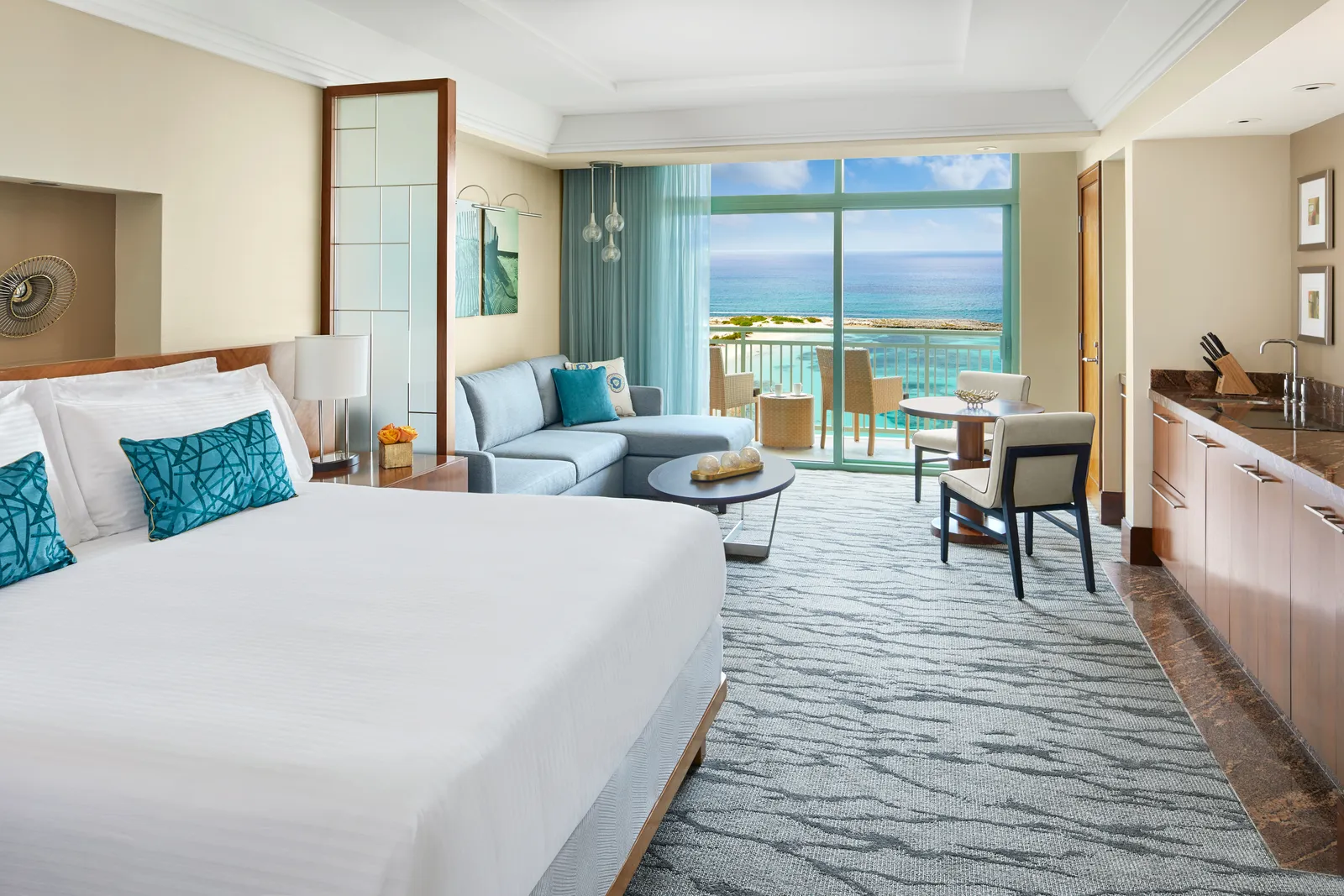 A studio at The Reef: the king bed, a sofa, the kitchen counter and a balcony over the sea.