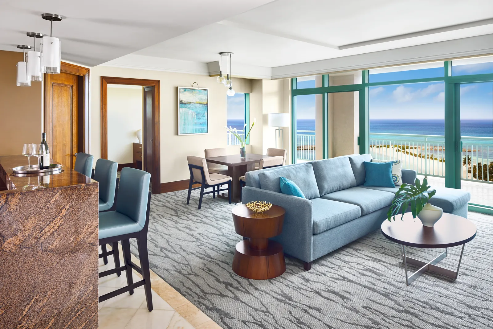 The living room of a Topaz suite, with a granite kitchen bar, a blue sofa and a window onto the beach.