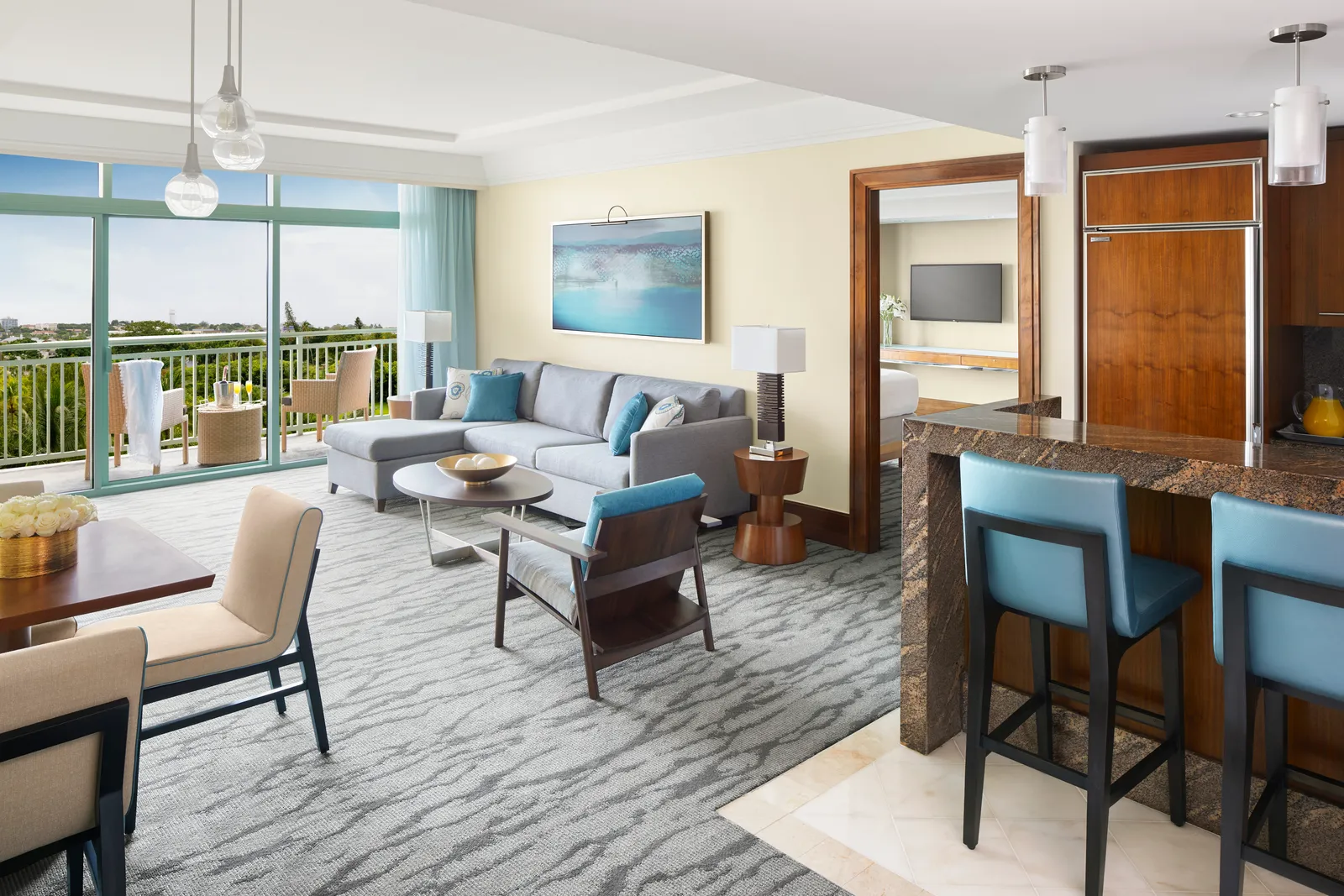 The living room of a suite at The Reef, with a grey sofa, a kitchen bar with stools and a balcony.