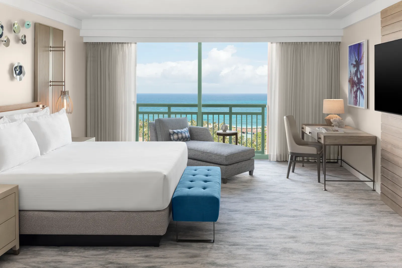 The bedroom of a Grand suite, with a king bed, a chaise longue, a desk and the sea beyond the window.