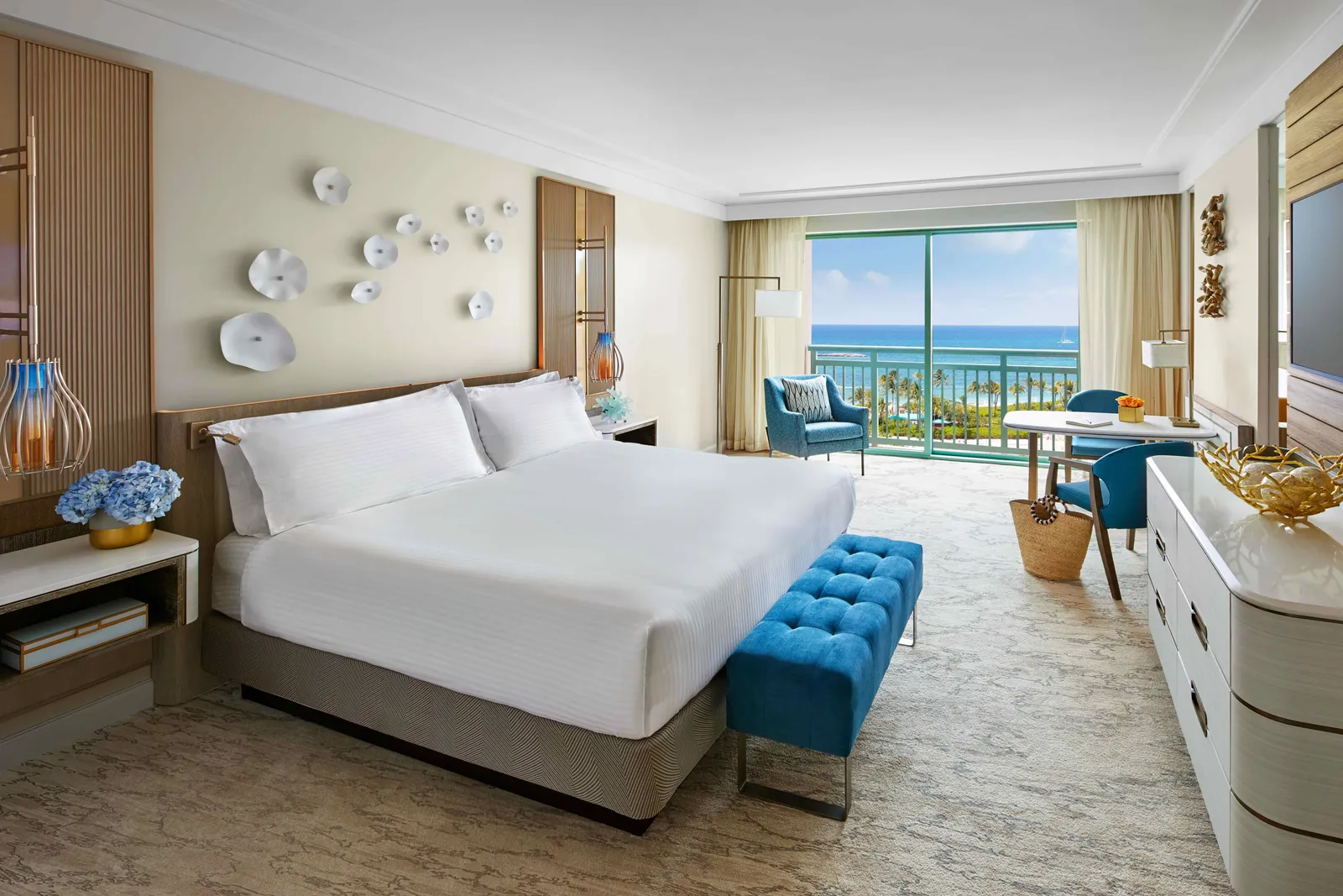 A room at The Royal with a king bed, blue armchairs and a full-height window onto the sea.