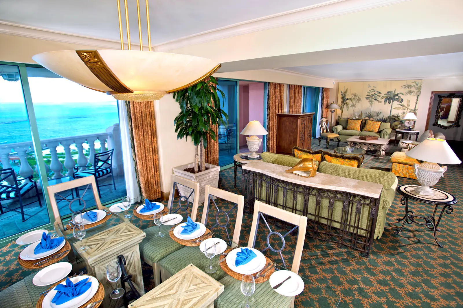 The living room of a Presidential suite at The Royal: a laid dining table, sofas and a balustraded terrace over the sea.