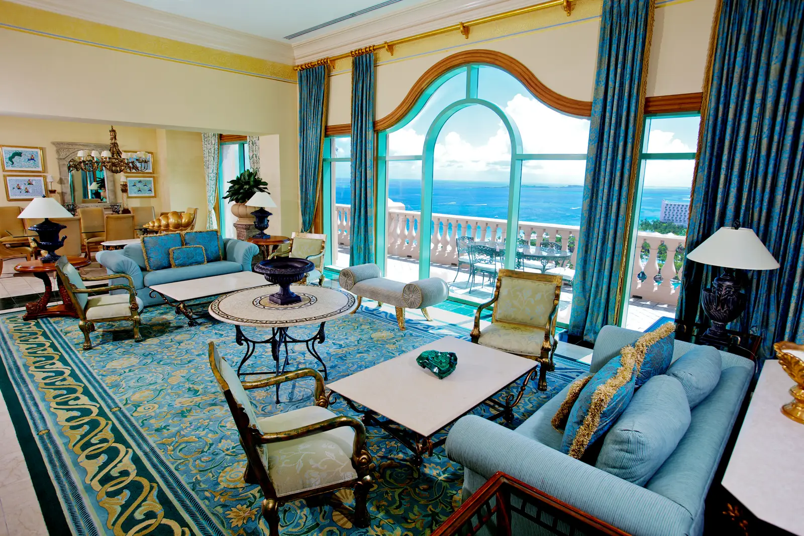The Royal Suite’s drawing room, with blue sofas, a patterned carpet and a tall arched window onto the terrace and the sea.