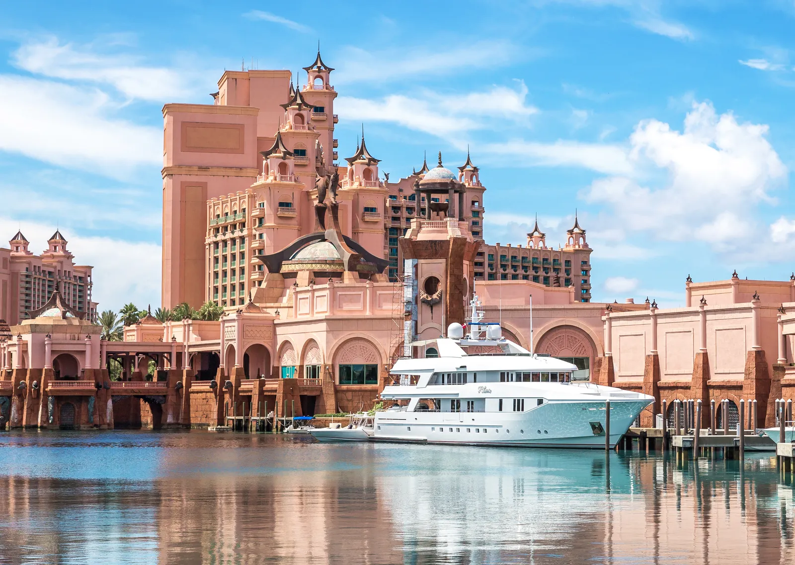 A white yacht moored in the marina beneath the pink towers and spires of The Royal.