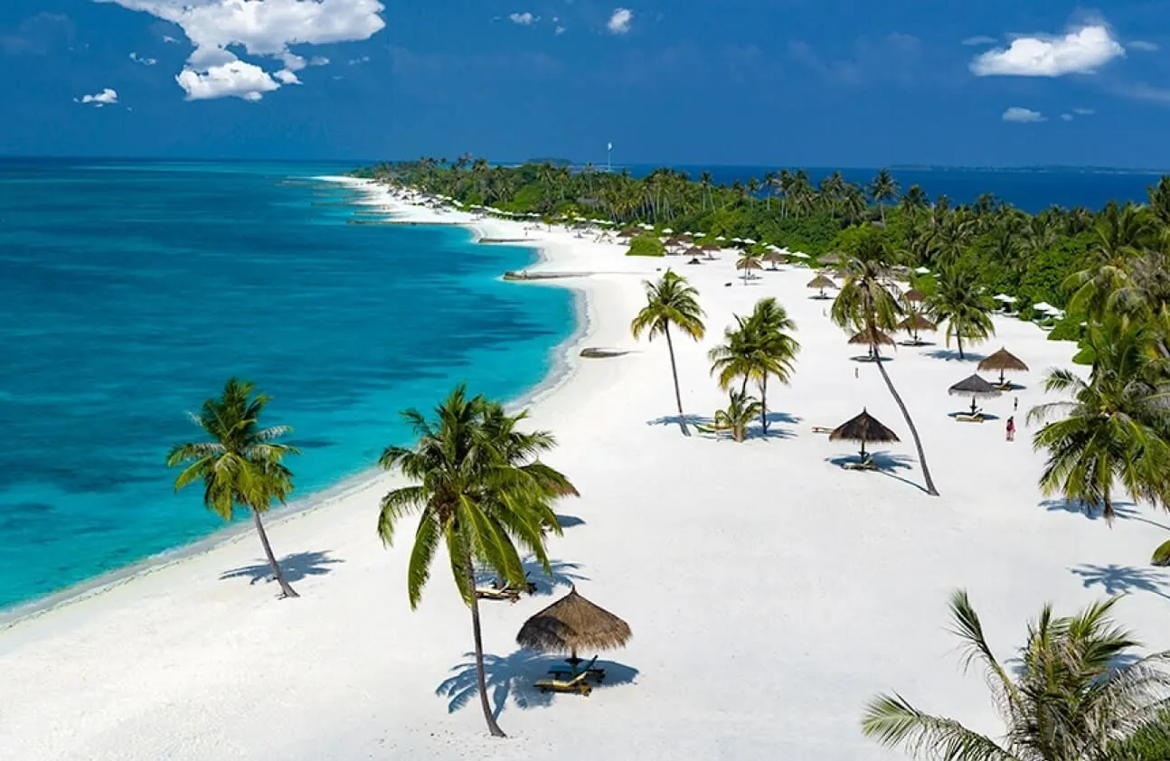 Kanifushi’s beach among leaning palms, turquoise water and a thatched umbrella