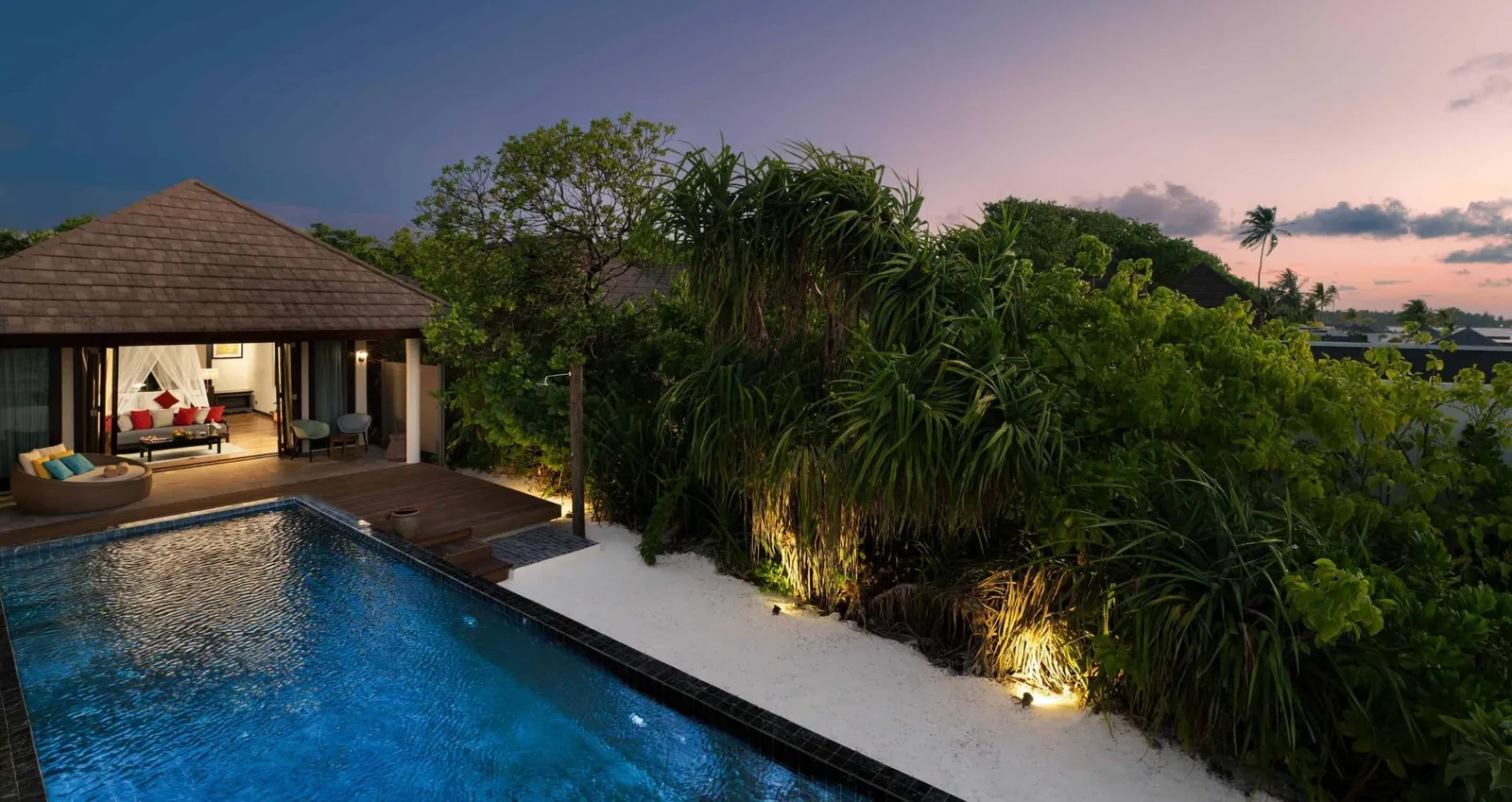 A Kanifushi Beach Villa’s long pool at dusk, the garden lit