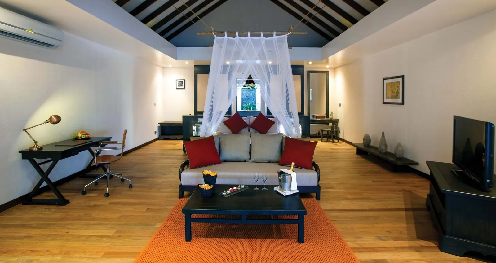 A Sunset Beach Villa’s living room, the red sofa and the bed under its net