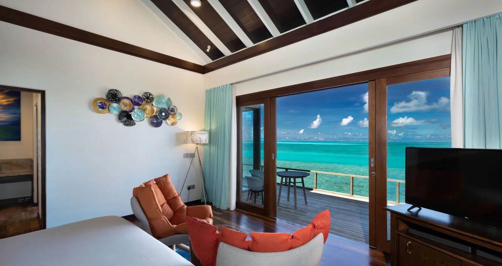 A Water Villa bedroom, its glass doors on the lagoon and the deck