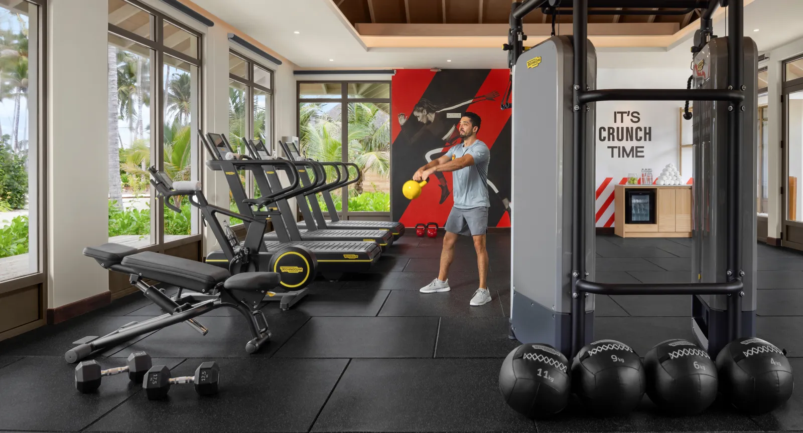 The gym: weights, machines and windows onto the palms; a guest trains at the back.