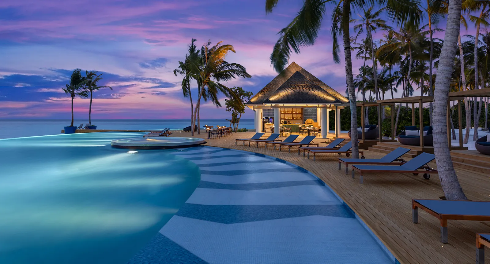 The Skipjack infinity pool at dusk, with loungers on the deck, the palms and the bar pavilion lit up.