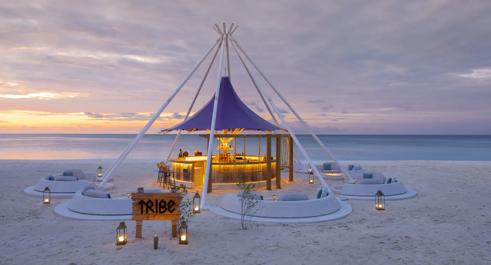 The Tribe beach bar at sunset: the peaked tent, the low sofas on the sand and the lanterns.