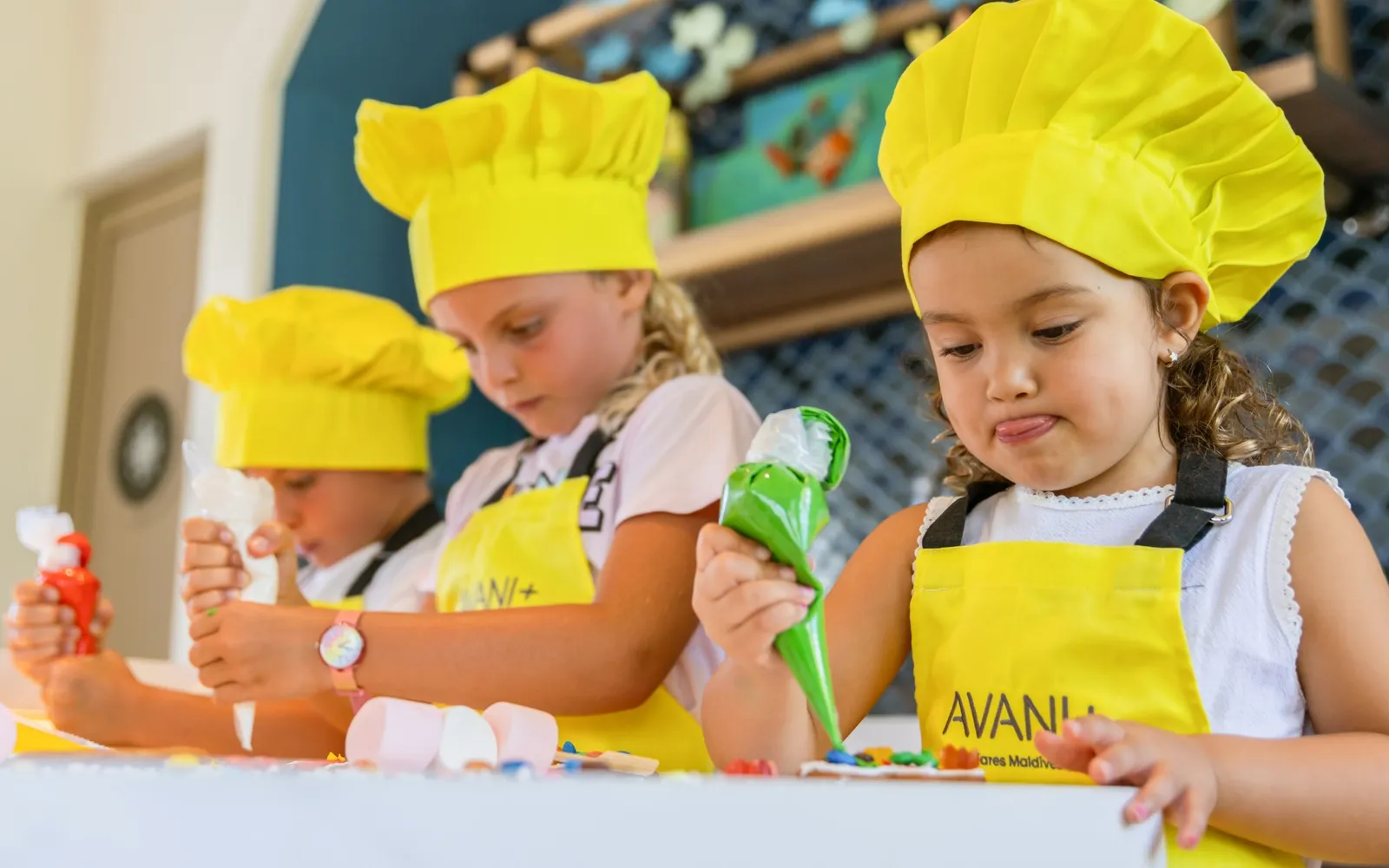 3 children in yellow chef’s hats decorate biscuits at Petit Bistro.