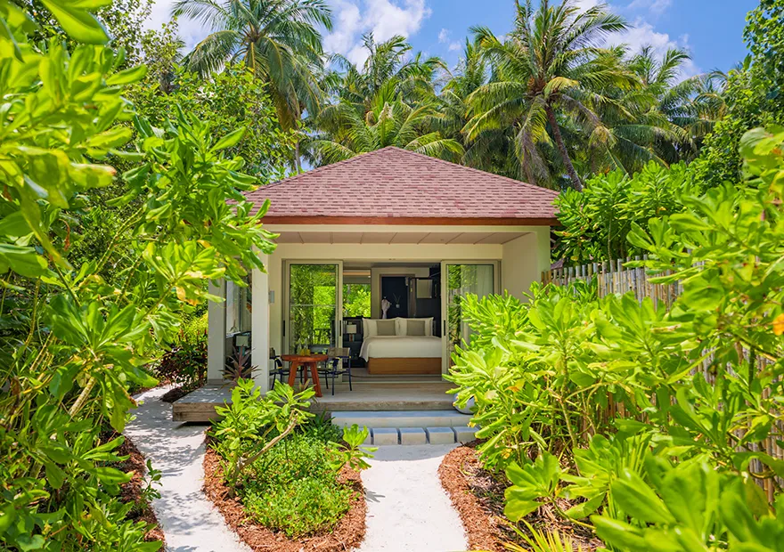 The Beach Villa seen from the sandy path through the greenery, its terrace and glass doors open.