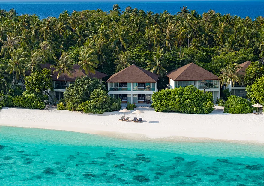 From above, three 2-storey pavilions in the greenery behind the beach and the shallows.