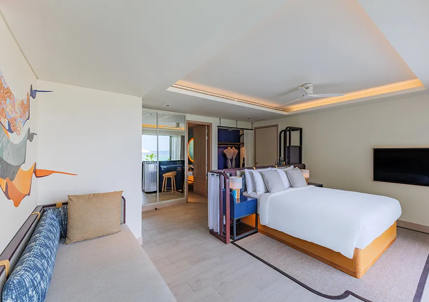 The Premium Beachfront Room: the bed, the window seat under the mural and the glass onto the green.