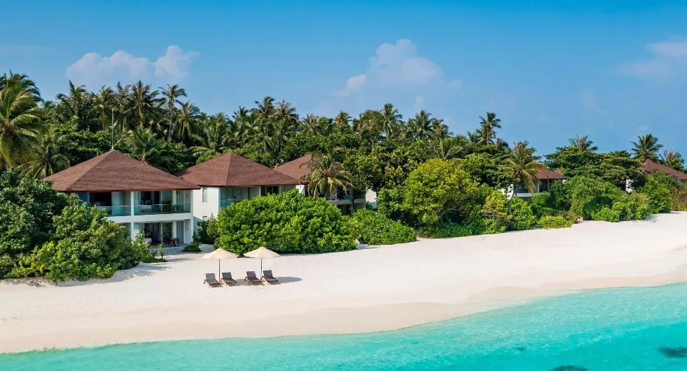 The 2-storey pavilions among the palms above the white beach and the lagoon, parasols on the sand.