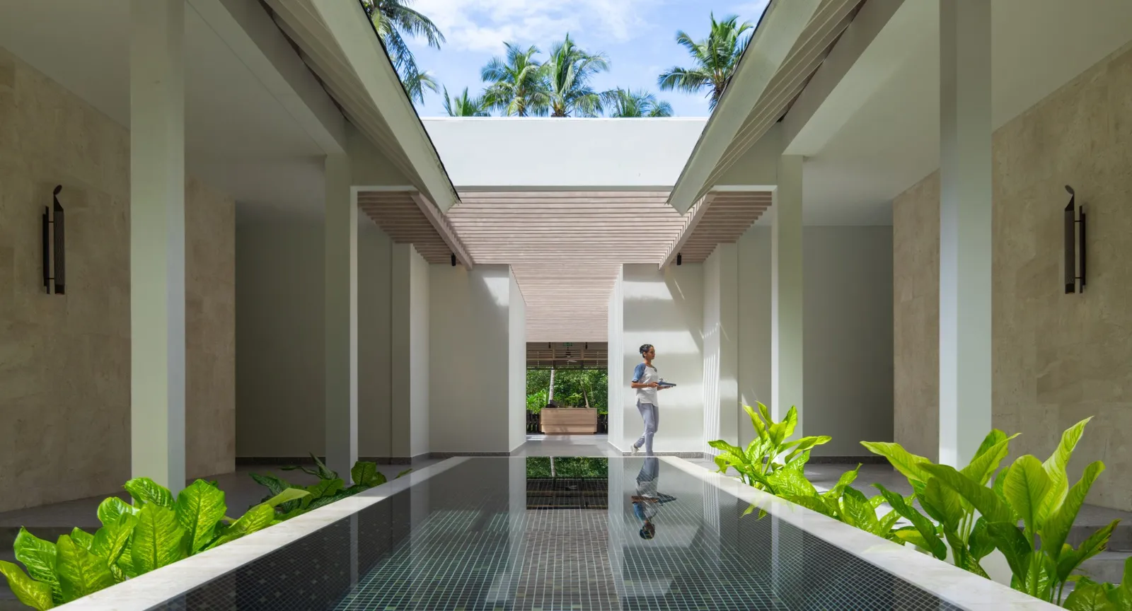 The spa entrance: a white open-air corridor with a dark pool of water and plants on either side.