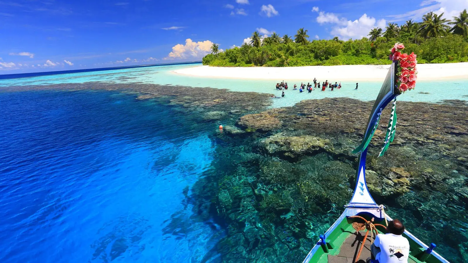 The bow of a dhoni nearing the island over the reef, the water clear to the bottom