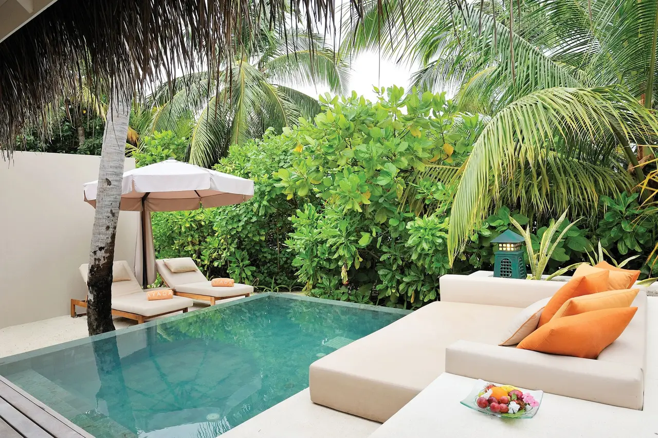A Beach Villa’s pool in its garden, orange cushions on the daybed