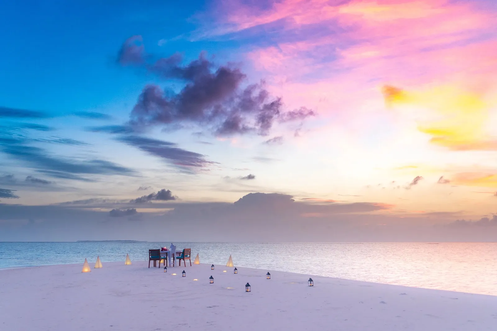 A table laid on a sandbank at sunset, among lanterns