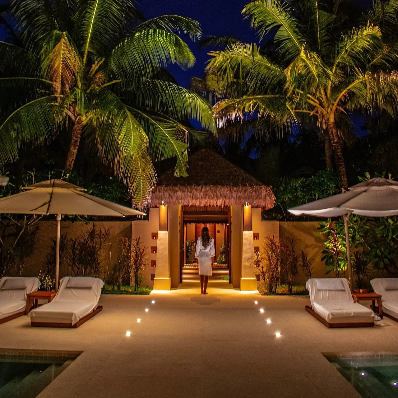 The AySpa entrance at dusk, lights in the ground and loungers among the palms