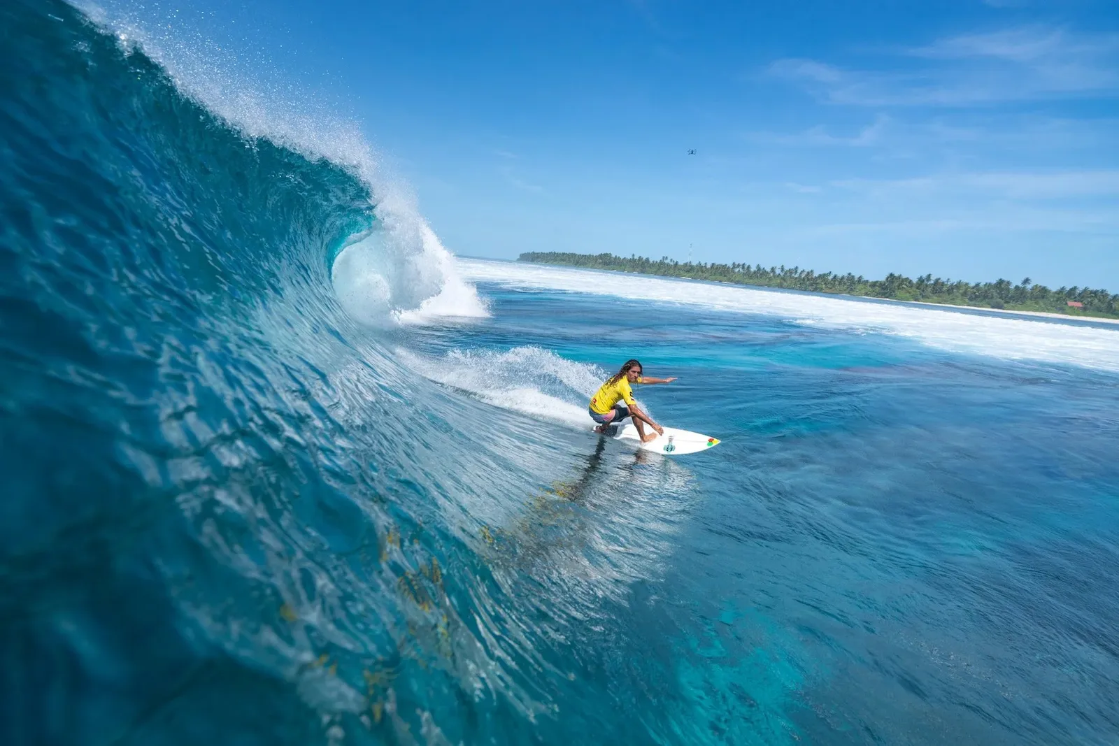 A surfer inside the curl of a wave, an island shore behind