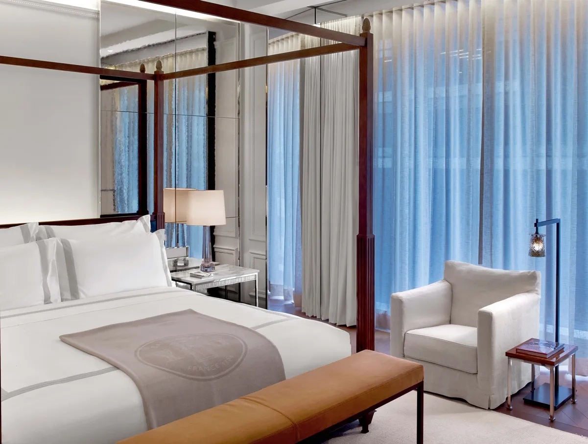 A wooden four-poster bed, white armchair and bench at the foot of the bed