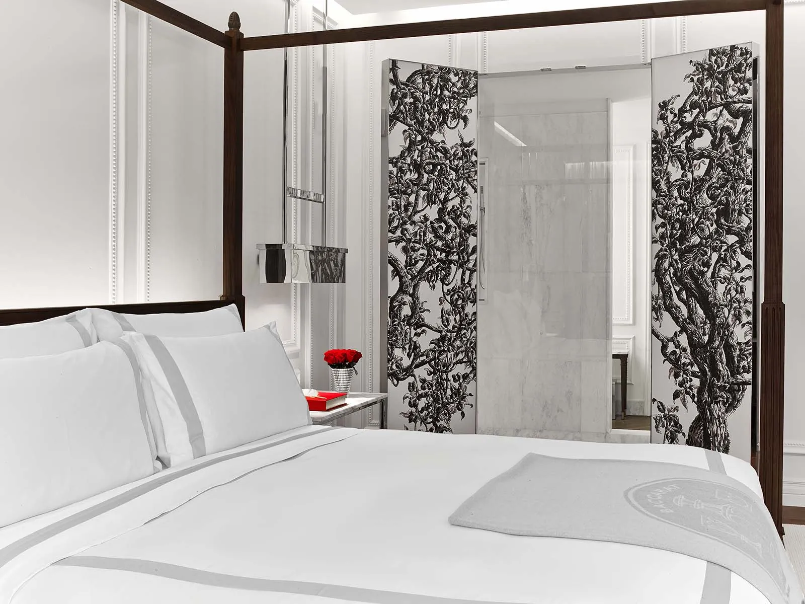 A four-poster bed and patterned panels opening onto a marble bathroom