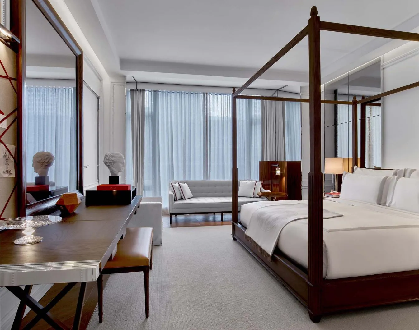 A four-poster bed, mirrored desk and sofa beside the windows